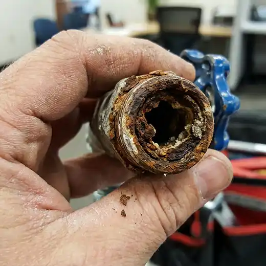 Close-up view of an old plumbing valve held by a hand, showing significant rust and mineral scale buildup that has heavily constricted the interior water passage.