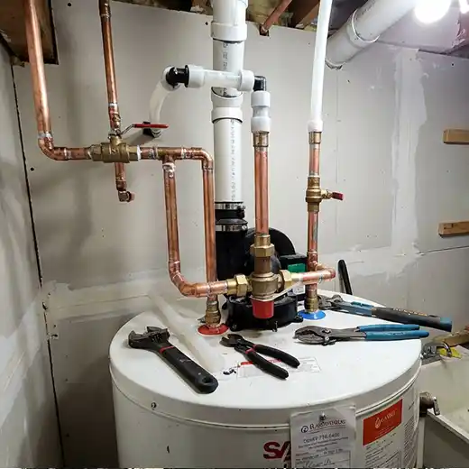 Residential water heater installation featuring complex copper and PEX piping, various brass valves, and plumbing tools like wrenches and pliers resting on top of the white tank.